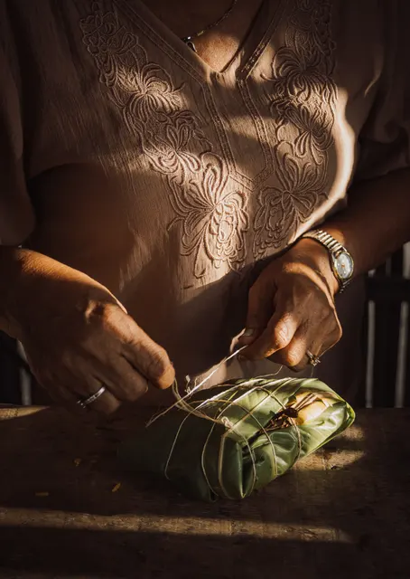 Manos envolviendo una preparación tradicional en hojas
