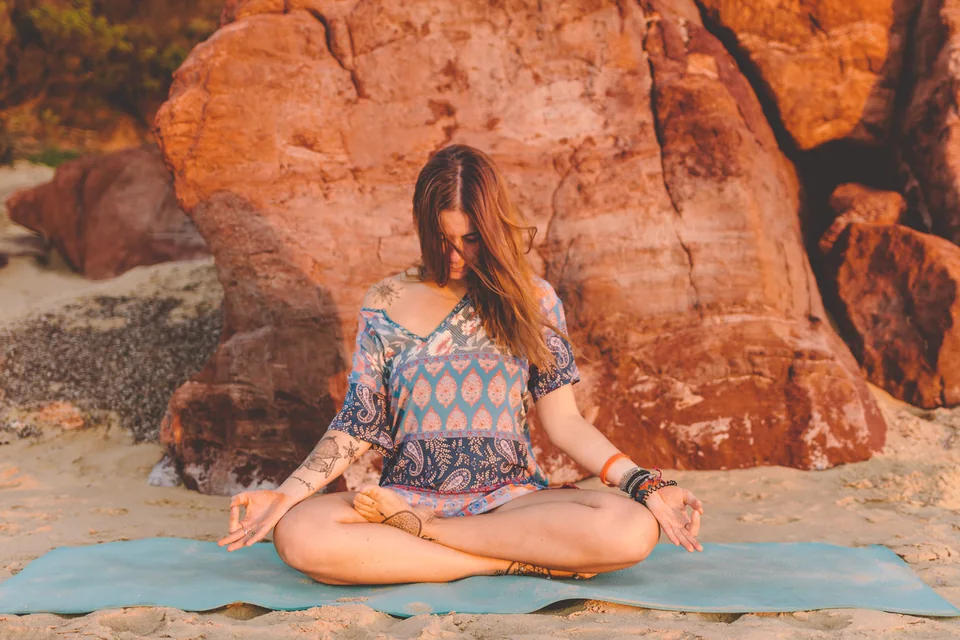 Mujer sentada en una postura de yoga sobre una esterilla al aire libre